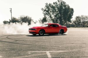 A vibrant red muscle car performing a drift, creating smoke on an open asphalt area in Sacramento, CA.