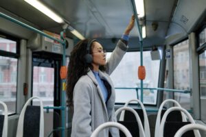 A woman with headphones stands inside a bus, enjoying music.