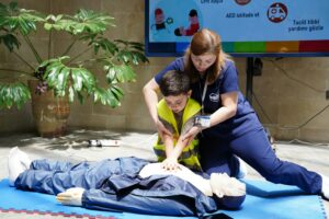 Nurse guides child in CPR training using a dummy indoors.